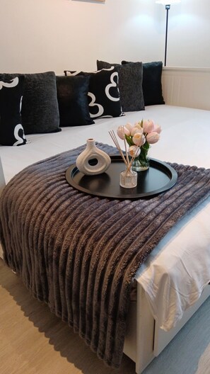 A neatly made bed with a brown textured blanket, a tray with a vase of flowers and reed diffusers, and black and white patterned pillows. - Borough Market, Tower Bridge, Shard, Central London Family Stay (London)