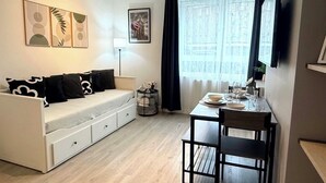 A modern, minimalist room with a white sofa, a dining table with chairs, a small side table, and artwork on the walls.