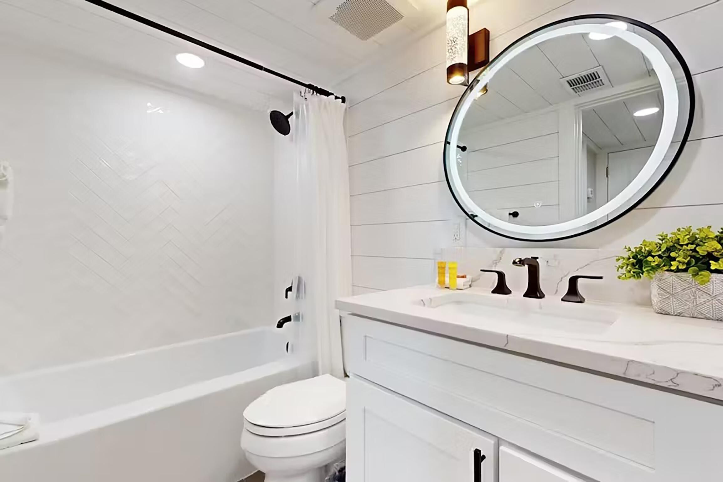 A modern bathroom with a white bathtub, toilet, and vanity with a mirror.