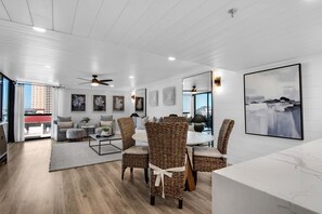 Een moderne woonkamer met een eethoek, met rieten meubels, een wit plafond en kunstwerken aan de muren.