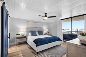 Een moderne slaapkamer met een groot bed, een plafondventilator, een nachtkastje met lamp en uitzicht op de stad door grote ramen.