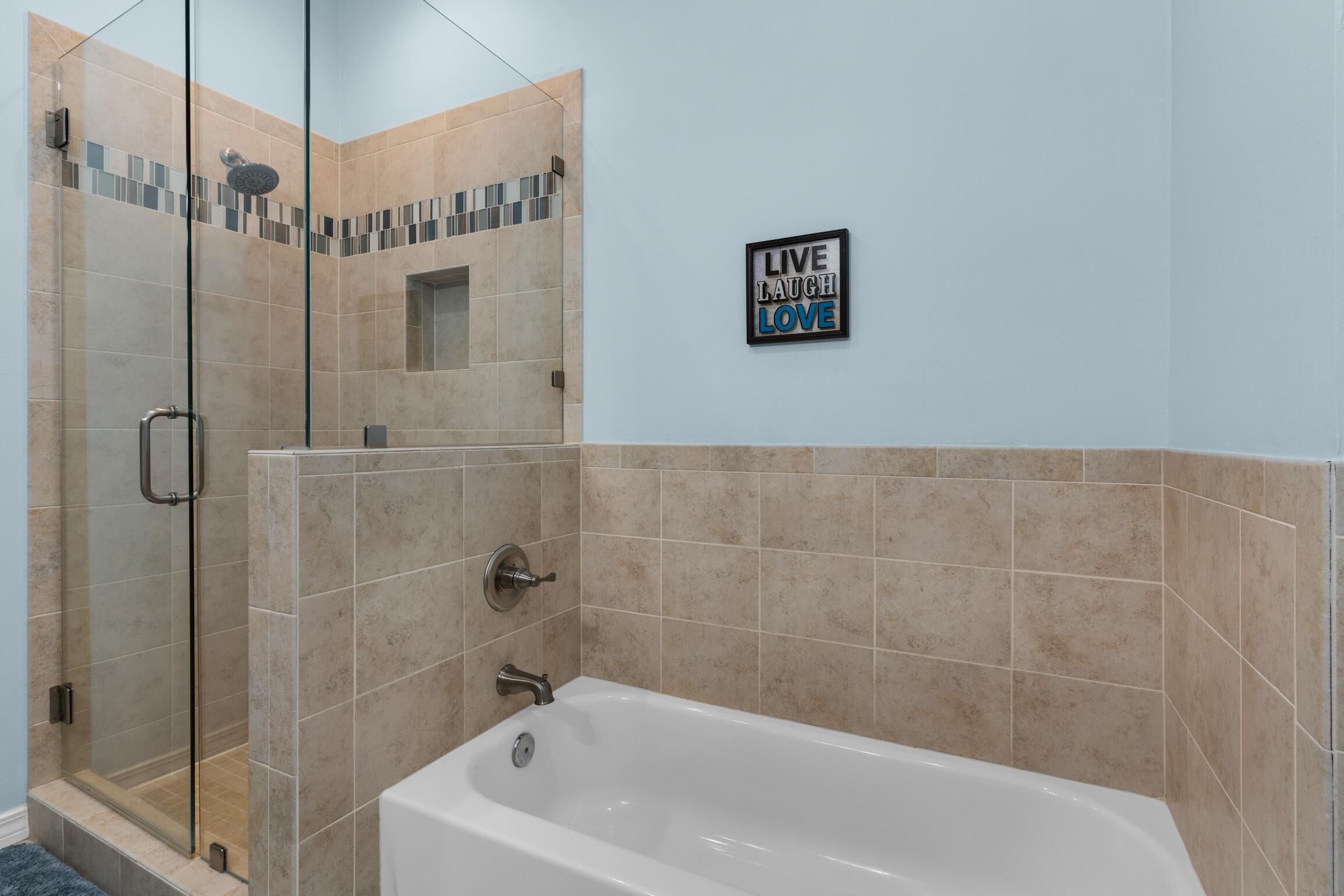 Un baño con cabina de ducha de vidrio, bañera y un letrero en la pared que dice 'Live Laugh Love'.
