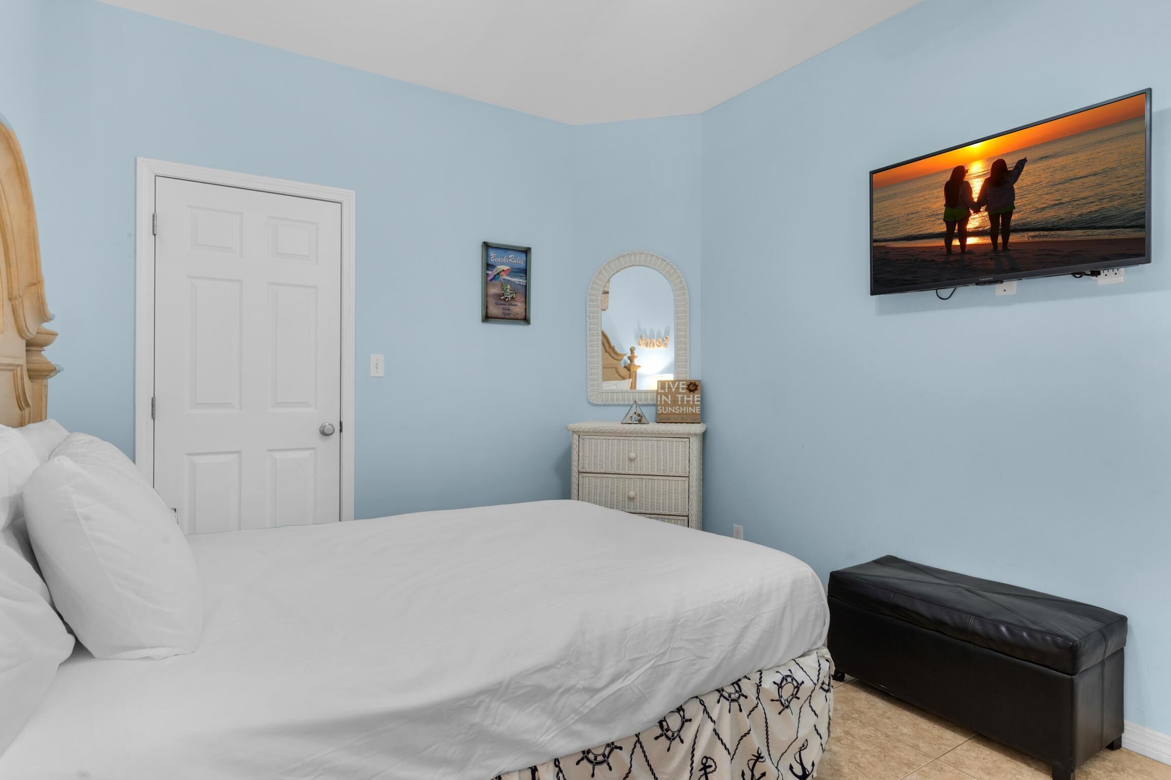Un dormitorio con cama, cómoda, espejo, televisor y maleta.