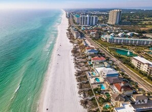 Vista aérea de un complejo turístico frente al mar, con propiedades en la playa, un gran hotel y un conjunto de piscinas.