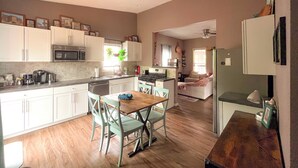 Une cuisine avec des meubles blancs, une table à manger avec des chaises, un four à micro-ondes, une cuisinière et un réfrigérateur.