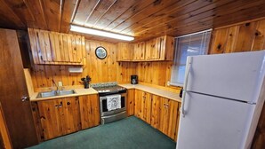 Une cuisine de taille réduite, dotée de meubles de rangement en bois, d’un évier, d’une cuisinière et d’un réfrigérateur.