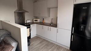 Een moderne keuken met witte kasten, een zwarte koelkast, een magnetron en een gasfornuis.