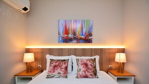 A neatly made bed with floral pillows, two bedside lamps, and a colorful painting of sailboats on the wall. - Villes de France - Centro de Floripa (Florianopolis)