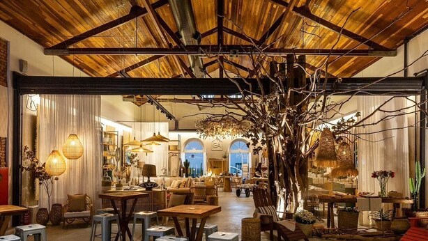 A spacious interior with high ceilings, exposed beams, and a central tree sculpture. Tables and stools are arranged for dining or socializing. - Villes de France - Centro de Floripa (Florianopolis)