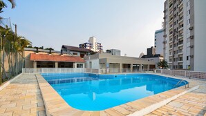 A swimming pool with a tiled deck, surrounded by buildings and a fence. - Villes de France - Centro de Floripa (Florianopolis)