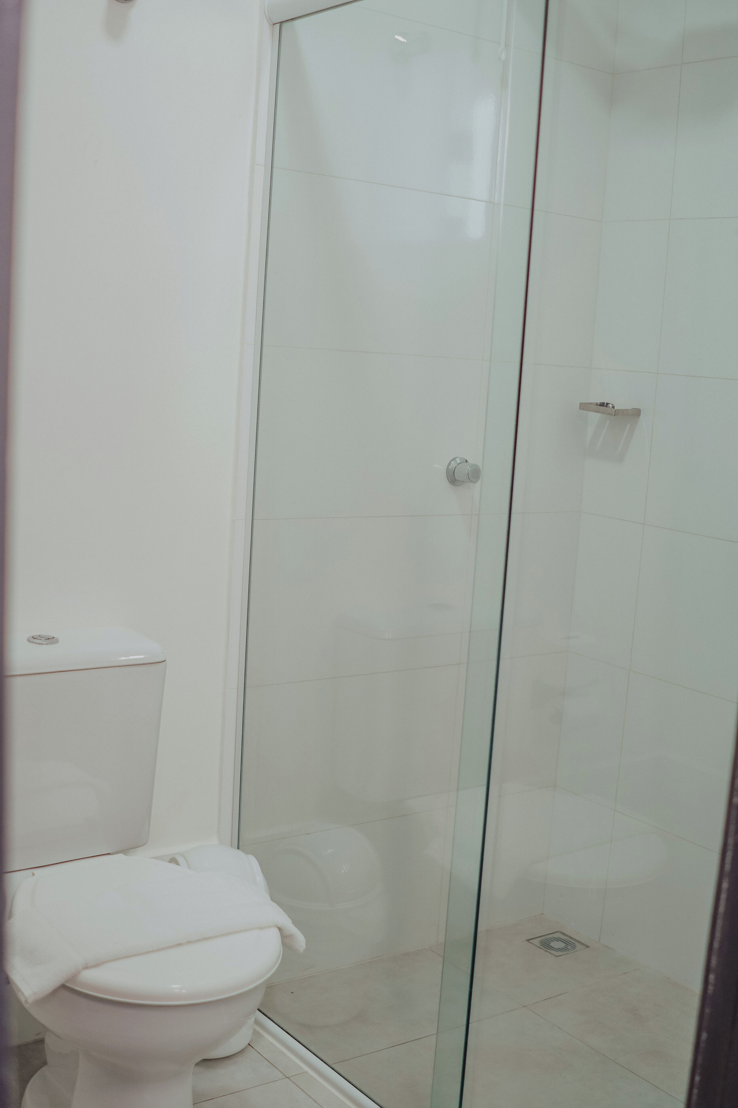 A bathroom with a toilet, a glass shower enclosure, and white tiled walls.