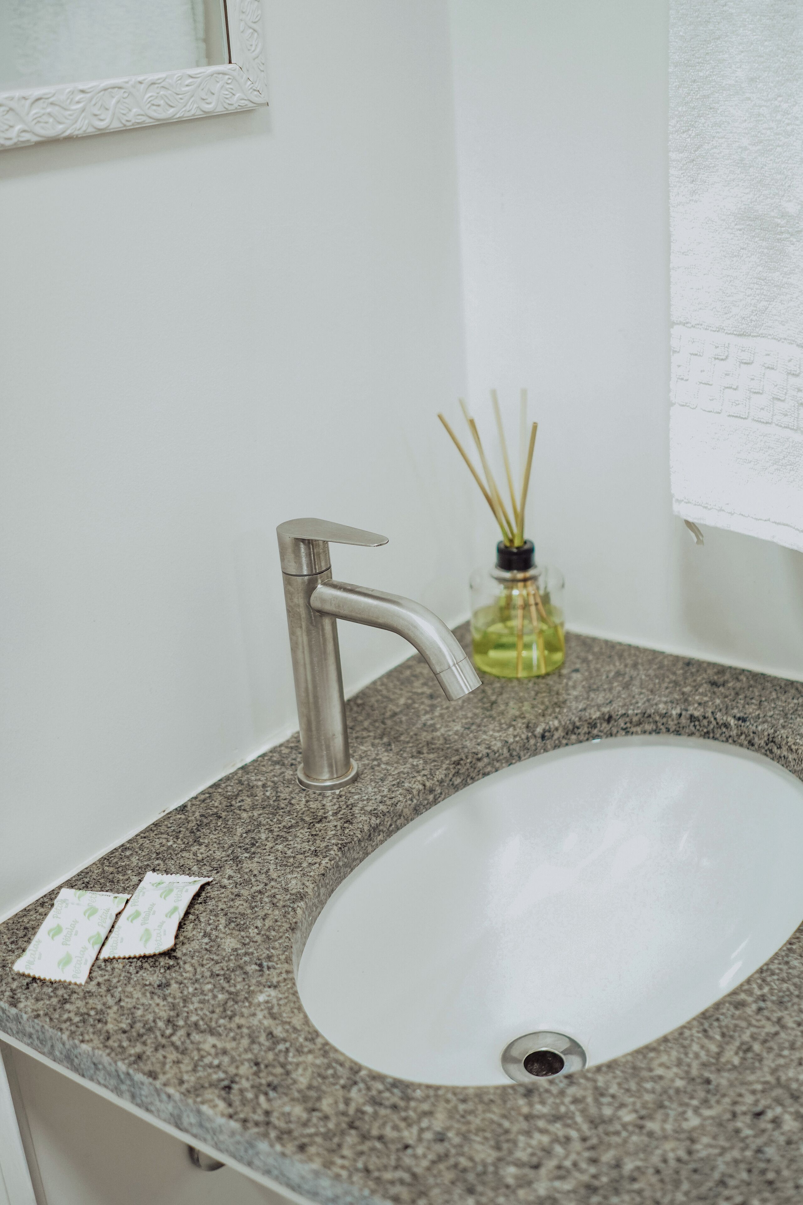 A bathroom with a white sink, a silver faucet, and a glass bottle with reed sticks.