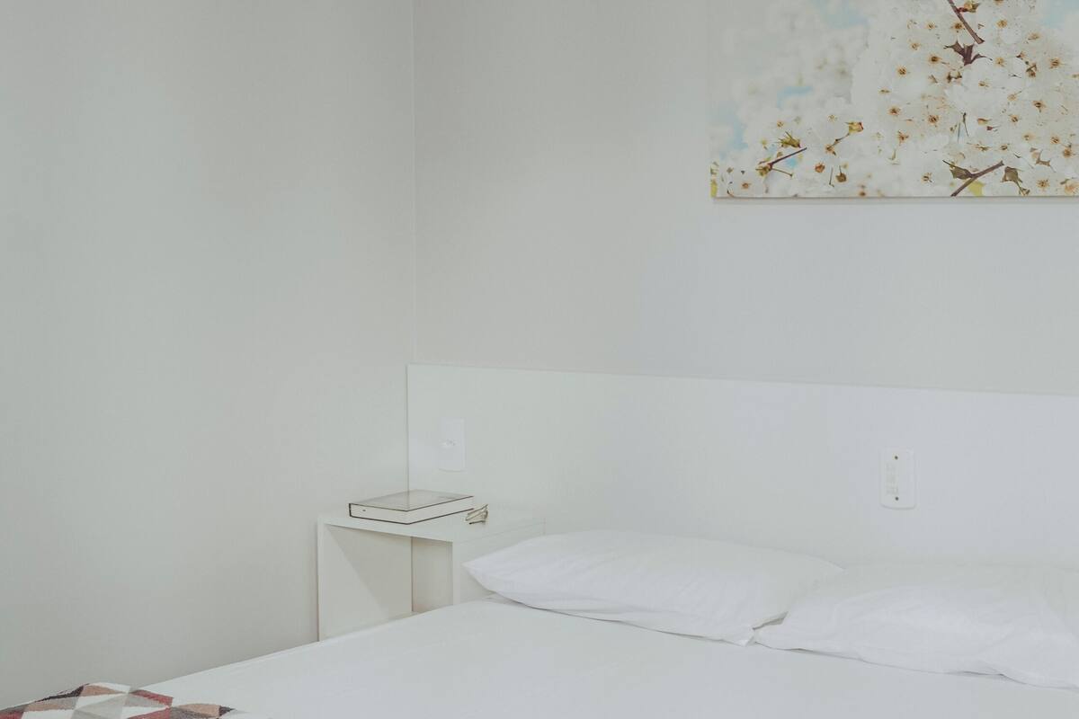 A bedroom with a bed, a ceiling fan, a nightstand, and a wall-mounted painting.