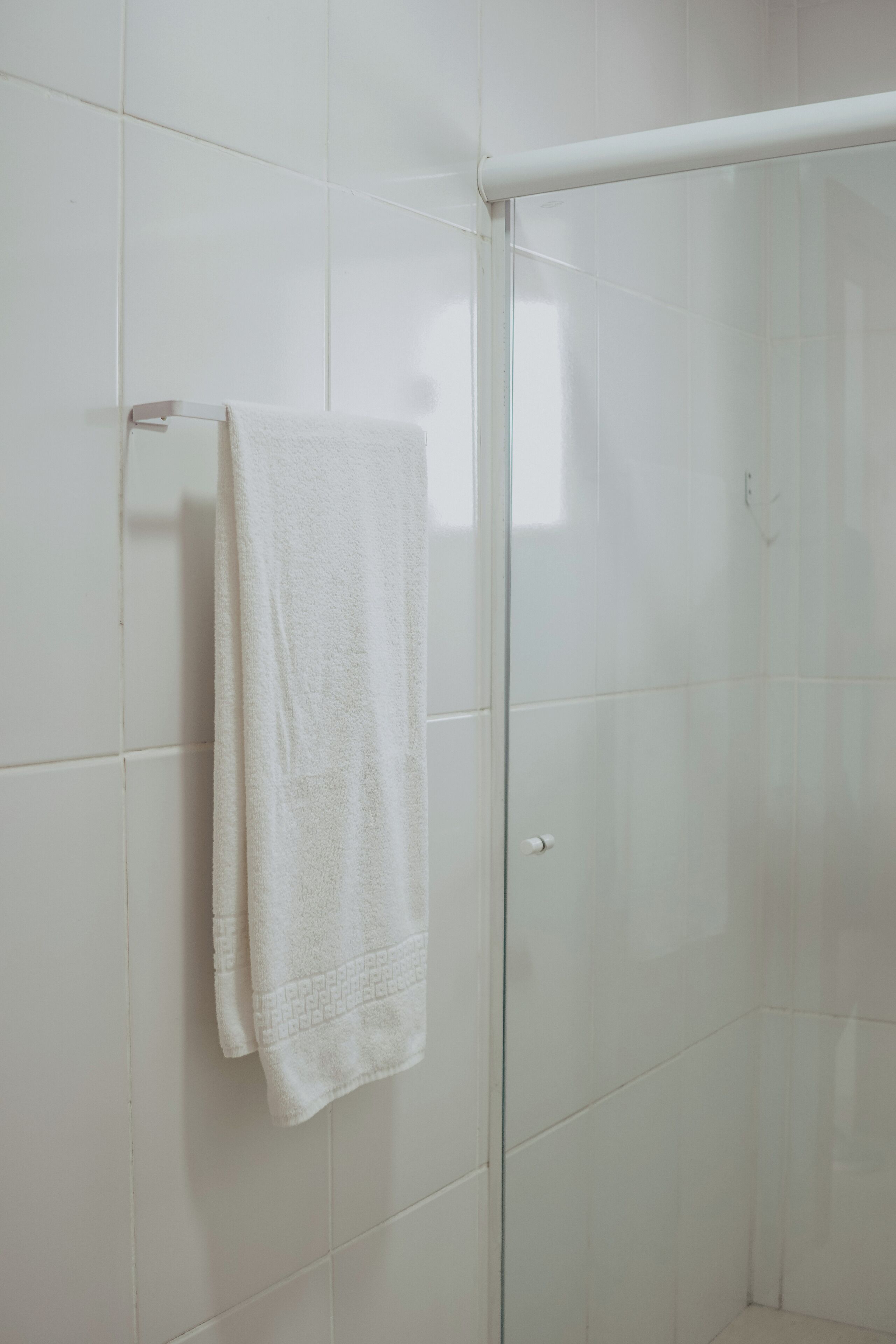 Un baño con paredes de azulejos blancos, una puerta de vidrio para la ducha y una toalla en un tendedero.