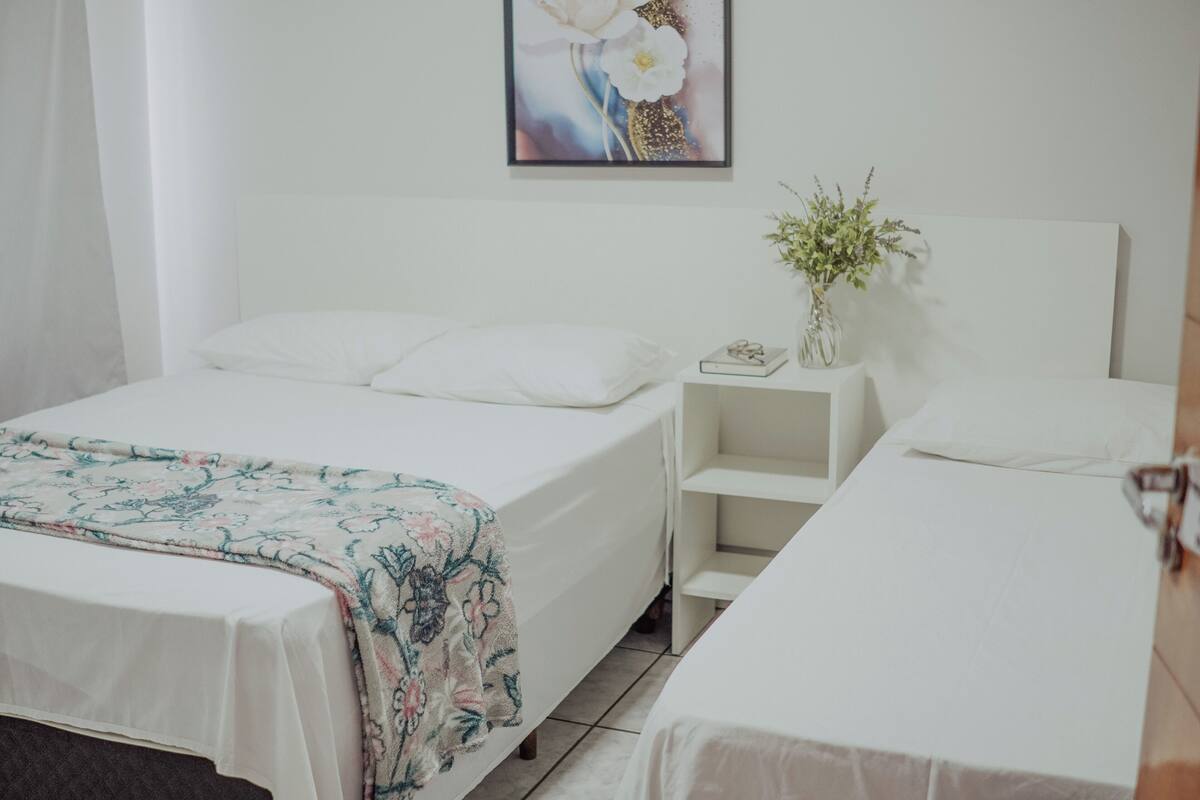 A hotel room with a single bed, a bedside table with a vase of flowers, and a painting on the wall.