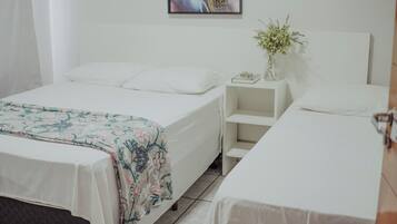 A hotel room with a single bed, a bedside table with a vase of flowers, and a painting on the wall.