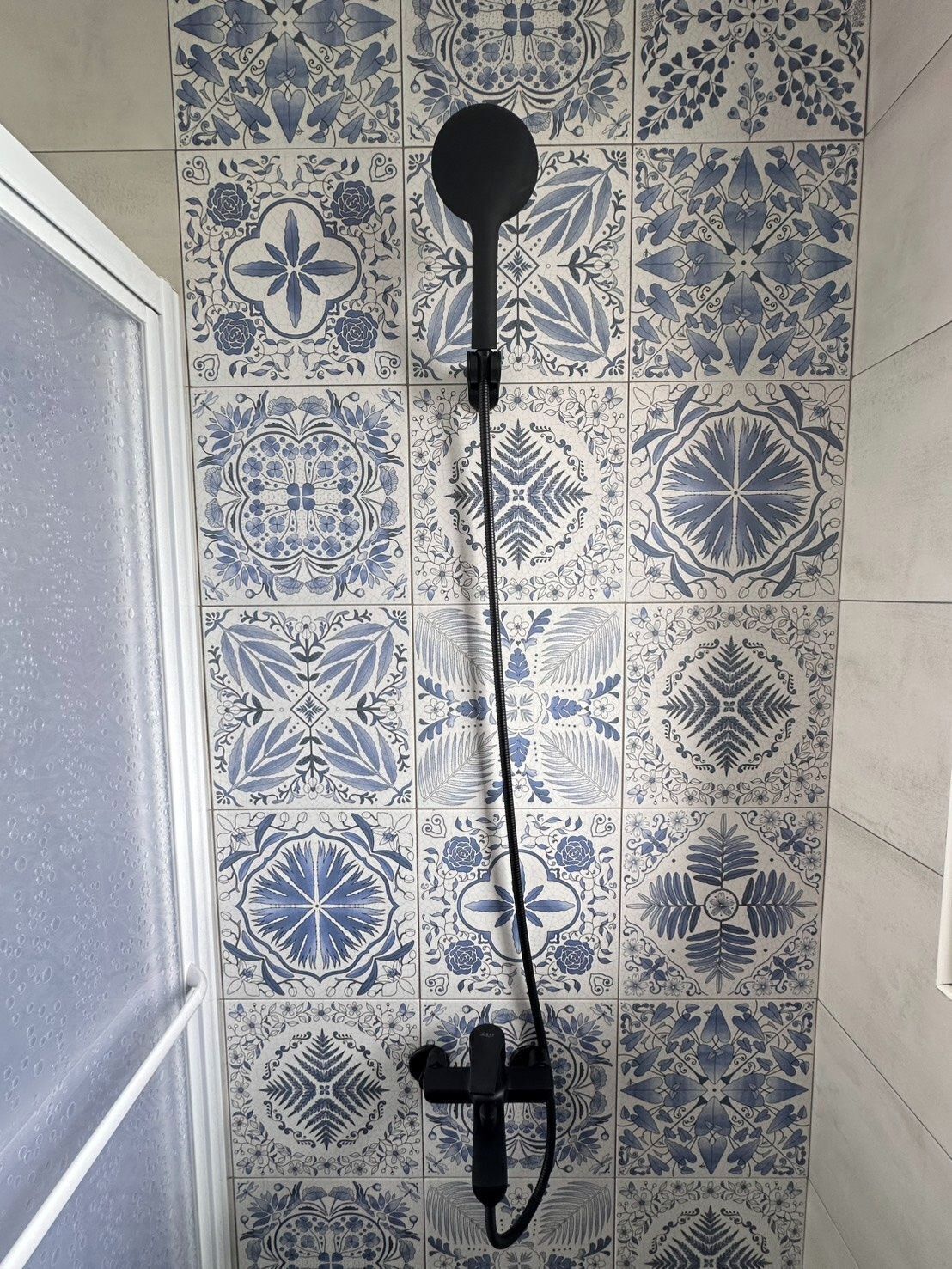 Eine Dusche mit einem schwarzen Schlauch und einer schwarzen Handbrause, die an einer Wand mit blau-weißen Fliesen angebracht ist.