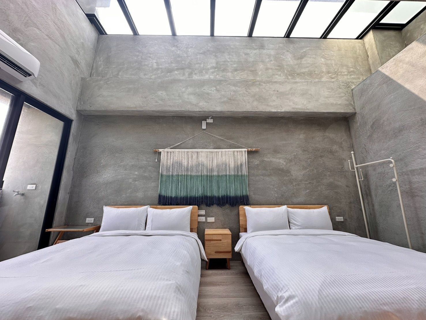 Ein modernes Schlafzimmer mit einer Dachfensterkuppel, zwei Betten, einem Wandteppich und einer Betonwand.