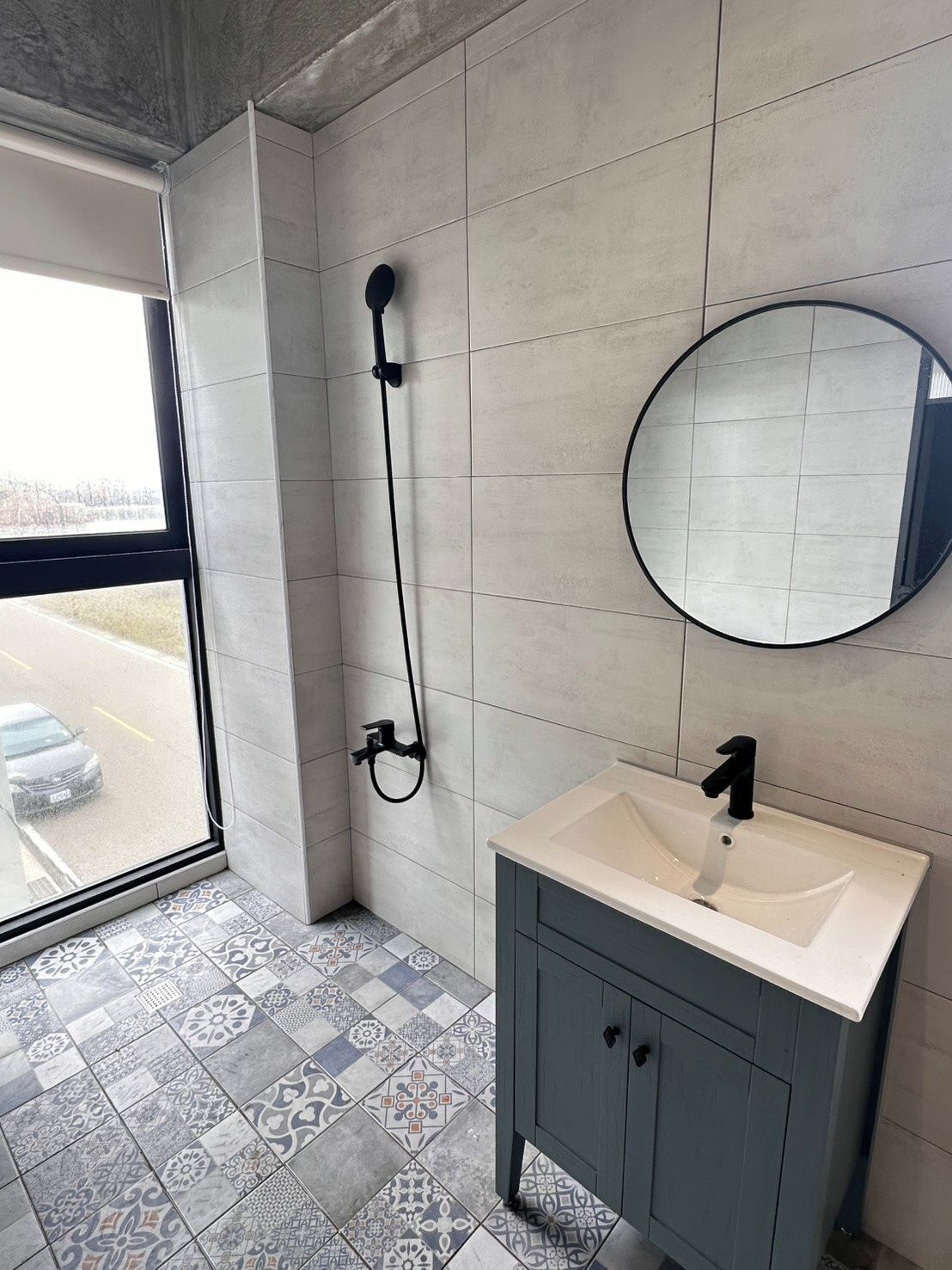 A bathroom with a shower, a sink, a mirror, and patterned tiles.