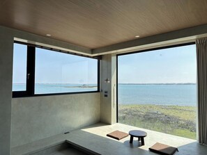 A modern room with large windows overlooking a body of water, a small table, and a bench. - SomeWhere Inn (Magong)