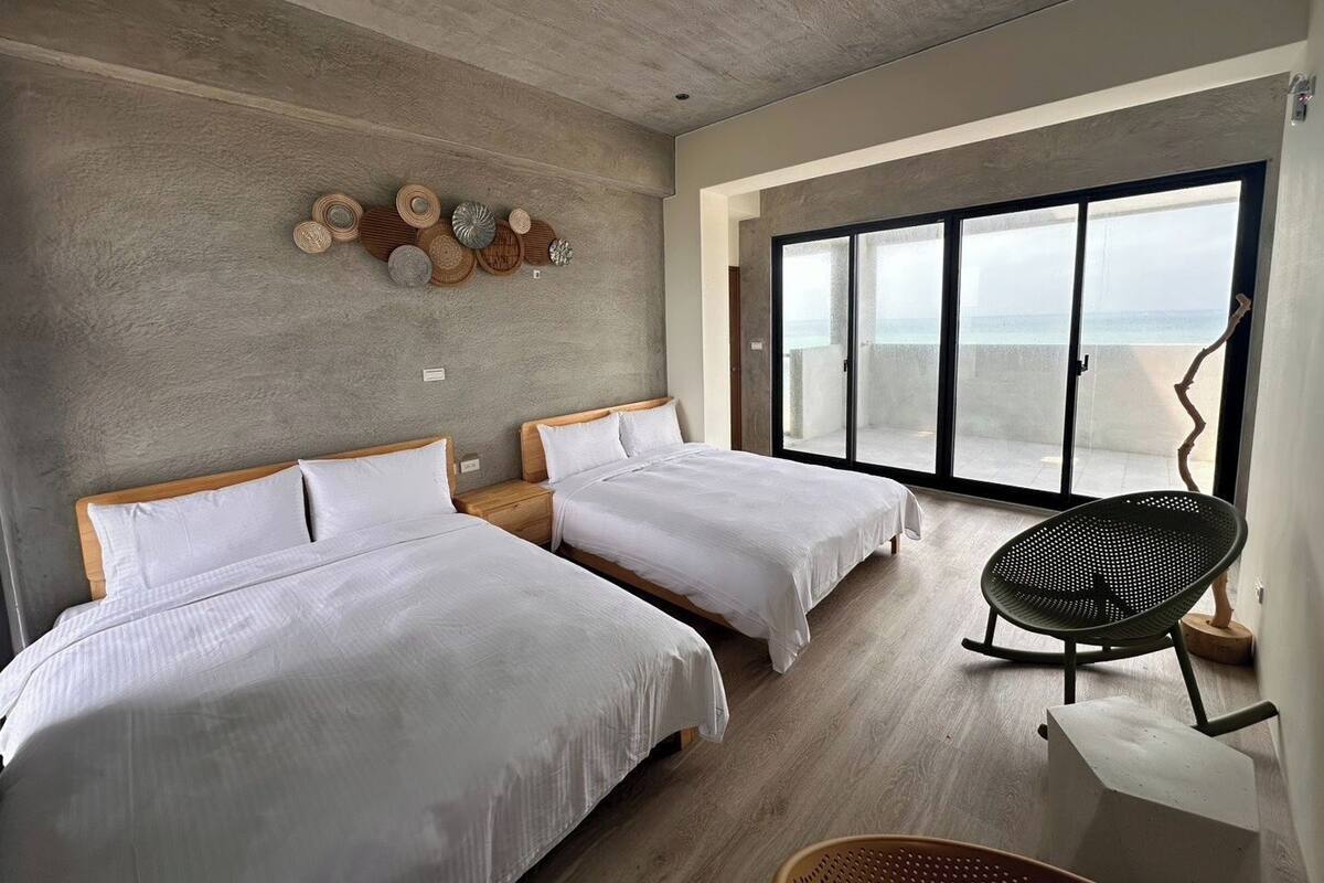 A modern bedroom with two beds, a large sliding glass door to a balcony, and a wall decorated with woven baskets.