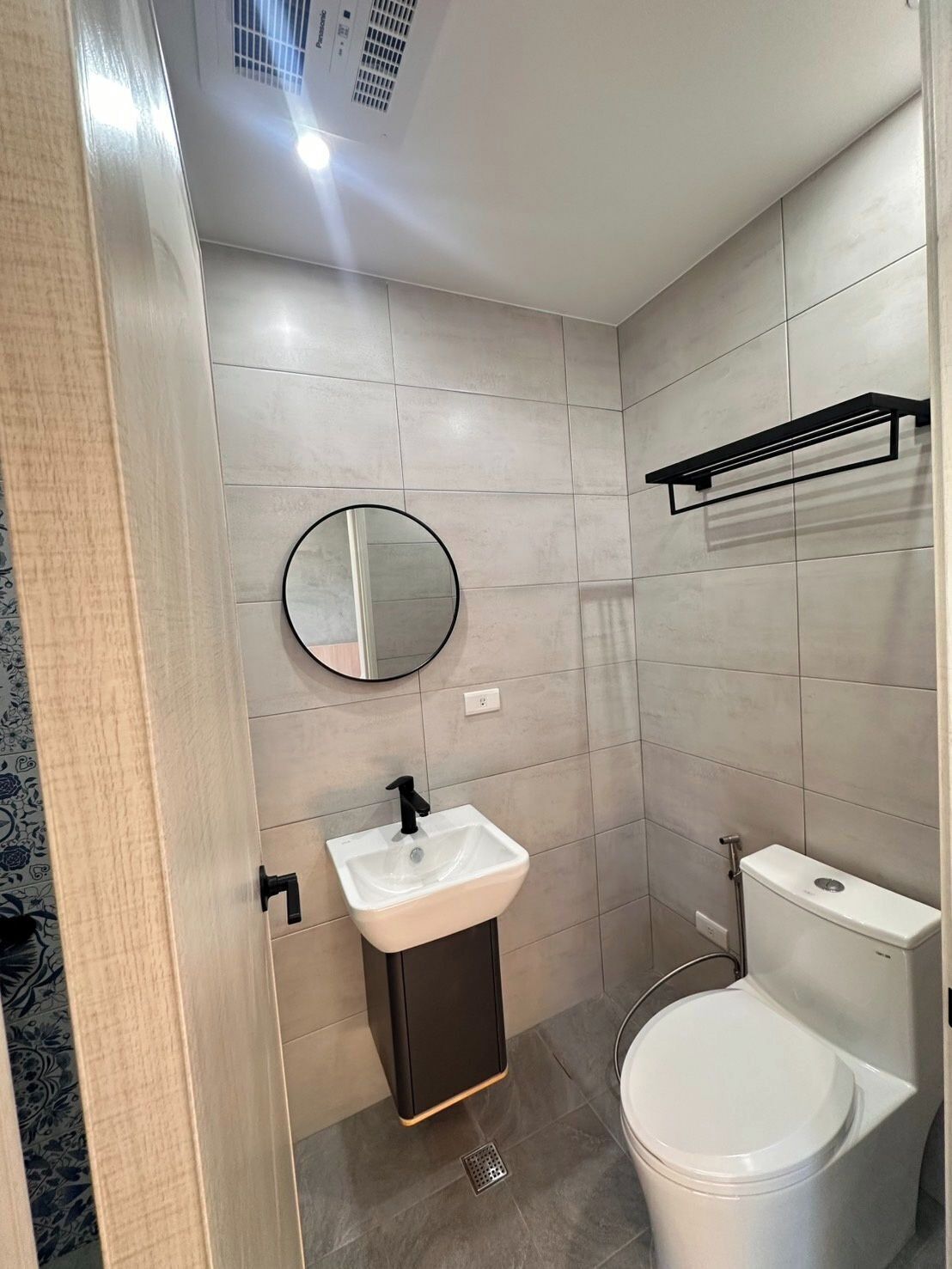 A modern bathroom with a white sink, black faucet, round mirror, and white toilet.