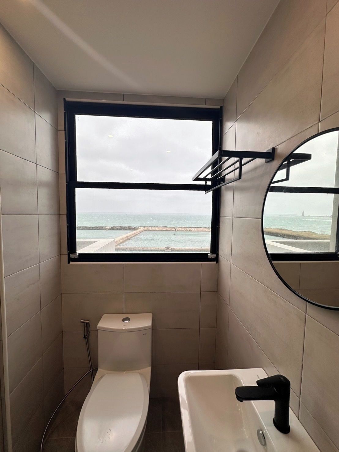 A bathroom with a toilet, sink, and a window with a view of the sea.