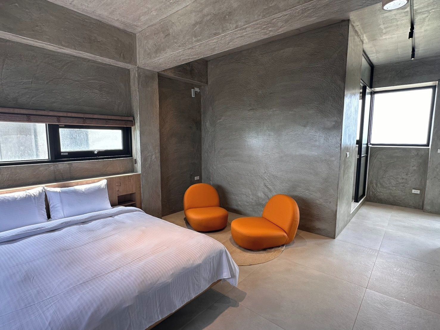 A modern bedroom with a bed, two orange chairs, a shower, and a large window.