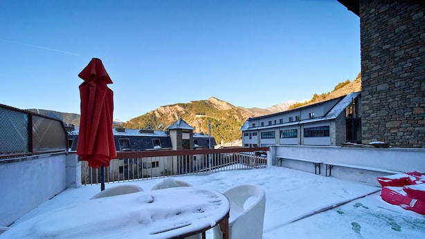 A snow-covered outdoor seating area with a table and chairs, a red umbrella, and a view of mountains in the background. - 𓃹 Bohemian Escape: Terrace, Parking by Ski Resort (Ordino)