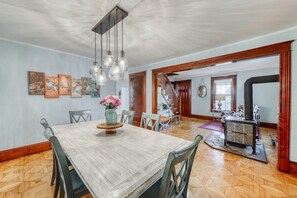 A dining area with a wooden table and chairs, a vase of flowers, and a staircase leading to another room. - The Farmhouse at South Hero (South Hero)