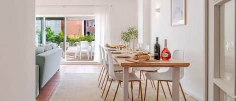A dining area with a table set for four, white chairs, a wooden table, and a bottle of wine on the table.