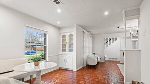 A spacious room with a white bench, a small round table, and a view of a blue car outside through a window. - Spacious yet cozy 4-bedroom house in a PRIME Location in Dallas! (Dallas)