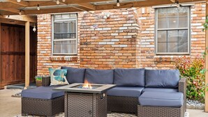 An outdoor seating area with a fire pit, wicker furniture, and a brick wall backdrop. - Spacious yet cozy 4-bedroom house in a PRIME Location in Dallas! (Dallas)