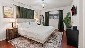 A bedroom with a large bed, a nightstand, a lamp, a painting, a mirror, a plant, and a TV on a stand. - Spacious yet cozy 4-bedroom house in a PRIME Location in Dallas! (Dallas)