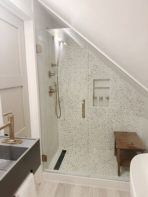 Ein modernes Badezimmer mit Dusche, einer Holzbank und einem kleinen Ablagefach für Toilettenartikel.