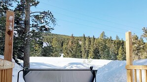 Un jacuzzi en un entorno nevado al aire libre, con una terraza de madera y vistas a un área boscosa.