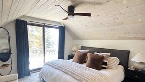 Un dormitorio con cama, mesitas de noche, ventilador de techo y un ventanal grande.