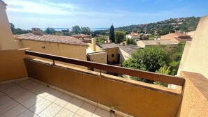 A balcony with a tiled floor and a railing, overlooking a residential area with houses and trees. - St Clair - Sea view apartment (Le Lavandou)