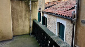 Un estrecho callejón con una valla de metal y un edificio con tejado de baldosas y contraventanas verdes.