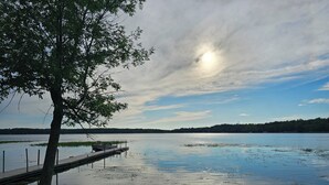Une vue sur le lac, avec une jetée s’avançant dans des eaux calmes, le tout entouré de prairies et d’arbres.