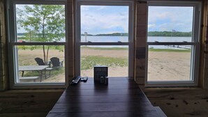 Une cabane en bois dotée de trois grandes fenêtres donnant sur une plage et un lac.