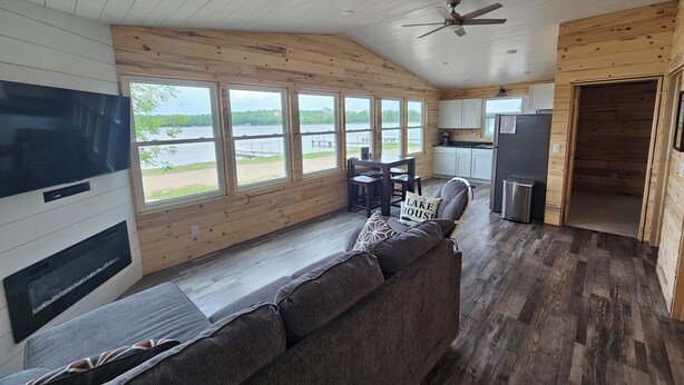 L’intérieur d’une cabane comprend un canapé, un téléviseur, des murs en bois, des fenêtres et un coin cuisine.