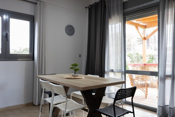 A dining area with a wooden table, white and black chairs, a small potted plant, and a view of an outdoor patio with a wooden pergola.
