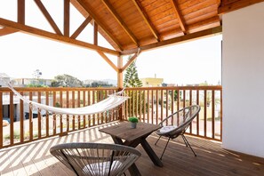 Una terraza de madera con una hamaca, dos sillas de mimbre y una pequeña mesa.