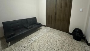 Een kamer met een zwarte bank, een houten deur en een zwarte tas op de vloer.