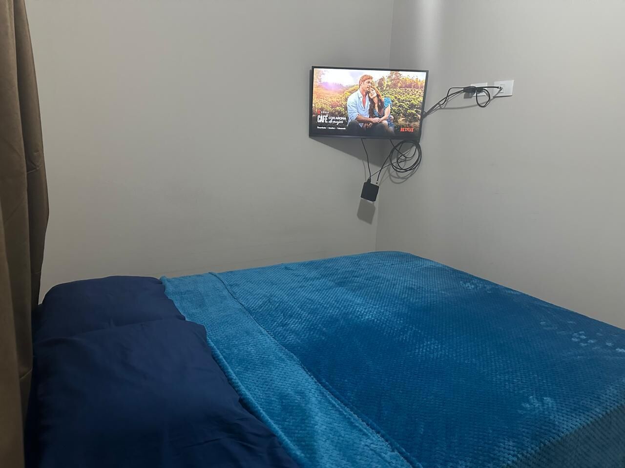 A single bed with a blue bedspread and a TV mounted on the wall displaying a show.