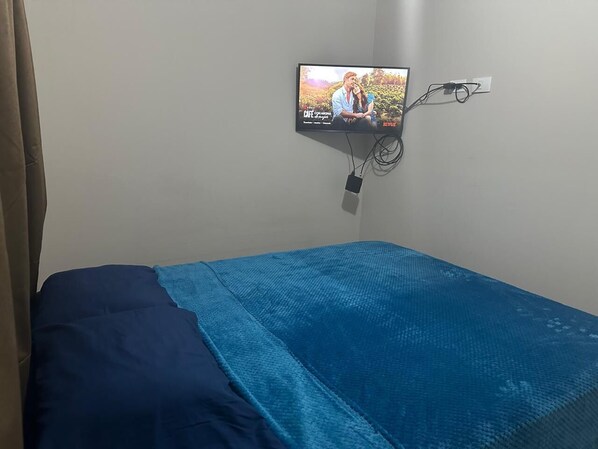 A single bed with a blue bedspread and a TV mounted on the wall displaying a show.