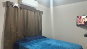 Een slaapkamer met een bed, bruine gordijnen, een aan de muur bevestigde televisie en een airconditioner in het plafond.