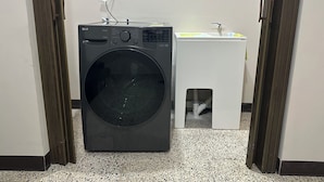 Een praktische wasruimte met een voorlader wasmachine, een klein wasbakje en een stopcontact op de muur.