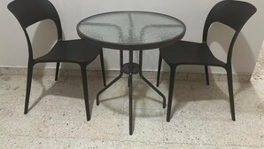 Een ronde glazen tafel met metalen poten, omringd door twee zwarte stoelen met gebogen rugleuningen.